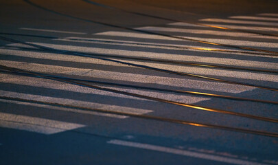 Steel tram tracks and white cross walk on asphalt road illuminated by street lights, closeup night photo