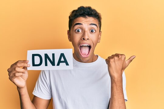 Young handsome african american man holding dna word pointing thumb up to the side smiling happy with open mouth