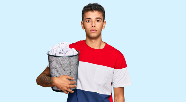 Young handsome african american man holding paper bin full of crumpled papers thinking attitude and sober expression looking self confident