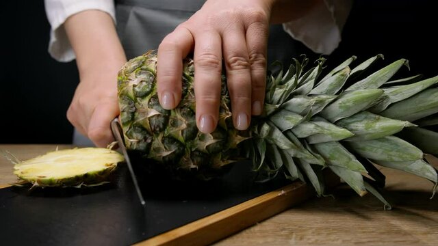 Female hands chopping pineapple on cutting board. Close up, 150 fps, slow motion