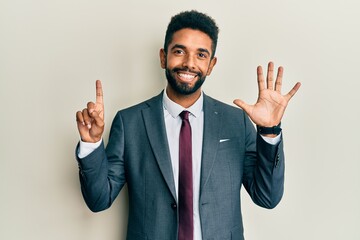Handsome hispanic man with beard wearing business suit and tie showing and pointing up with fingers...