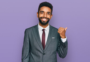 Young african american man wearing business clothes smiling with happy face looking and pointing to the side with thumb up.