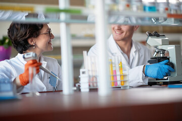 Young chemistry students are chatting while pipetting and microscoping in a laboratory. Science,...