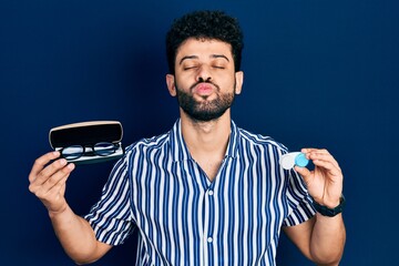 Young arab man with beard holding glasses and contact lenses looking at the camera blowing a kiss...