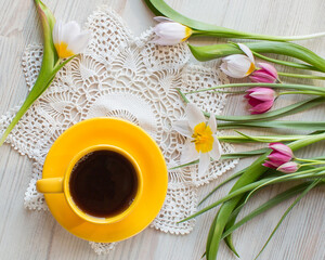 morning coffee in bright yellow cup, vintage napkin. Fresh garden pink and white tulips, spring flowers on white wooden background, top view from above,