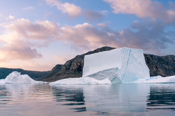 Big blue iceberg reflecting in water floats in the sea by Broughton Island, Nunavut, Canada. Boat ride from Inuit community of Qiqiktarjuaq later in the day. Soft glowing sky.