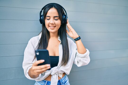 Young hispanic girl smiling happy using smartphone and headphones at the city.