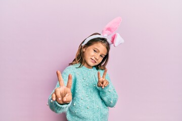 Little beautiful girl wearing cute easter bunny ears smiling looking to the camera showing fingers doing victory sign. number two.