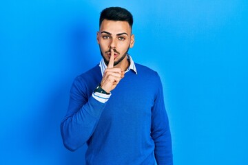 Young hispanic man with beard wearing casual blue sweater asking to be quiet with finger on lips. silence and secret concept.