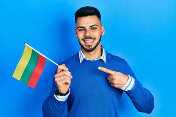 Young hispanic man with beard holding lithuania flag smiling happy pointing with hand and finger