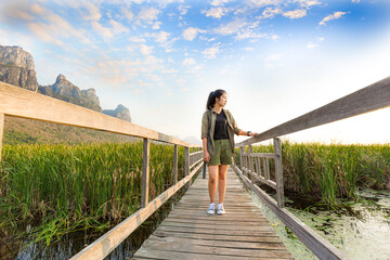 Asian hikers carry heavy backpacking on a small Pavilion outdoor hiking path on a wooden bridge in a swamp with meadows with a blue mountain background. Khao Sam Roi Yot National Park