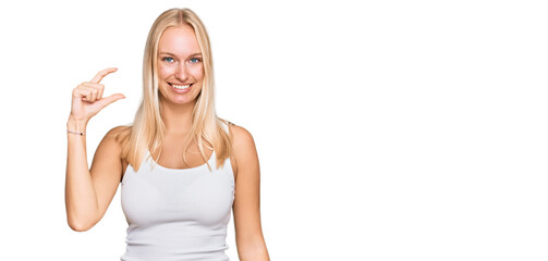 Naklejka na ściany i meble Young blonde girl wearing casual style with sleeveless shirt smiling and confident gesturing with hand doing small size sign with fingers looking and the camera. measure concept.