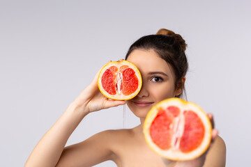 Beauty portrait of an attractive sensual brunette young woman smiling isolated over grey background, showing halves of grapefruit, Spa, beauty and cosmetic concept
