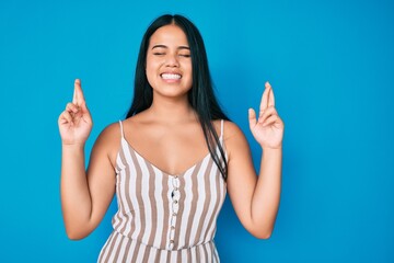 Young beautiful asian girl wearing casual clothes gesturing finger crossed smiling with hope and eyes closed. luck and superstitious concept.