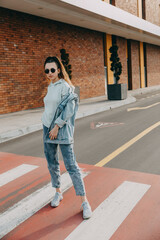 Young woman wearing 90s style denim clothes and round sunglasses on city street.