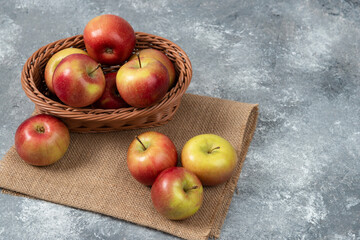 Wicker basket of ripe shiny apples on marble surface
