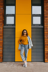 Young woman wearing jeans and a sweatshirt, on yellow wall background.