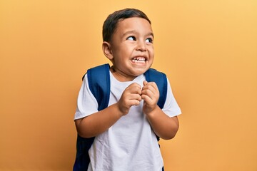 Adorable latin toddler smiling happy wearing student backpack over isolated yellow background.