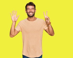 Fototapeta premium Handsome young man with beard wearing casual tshirt showing and pointing up with fingers number seven while smiling confident and happy.
