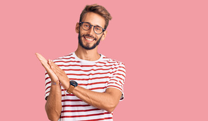 Handsome blond man with beard wearing casual clothes and glasses clapping and applauding happy and joyful, smiling proud hands together