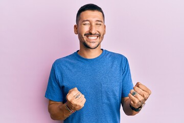 Handsome man with tattoos wearing blue tshirt clothes celebrating surprised and amazed for success with arms raised and eyes closed