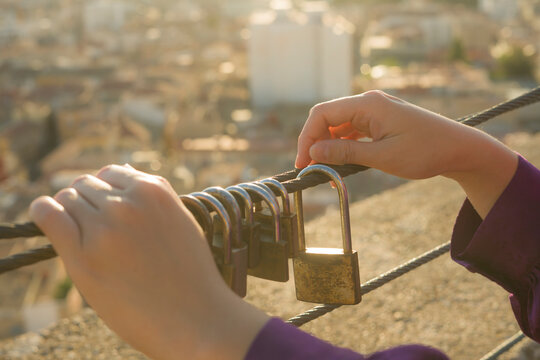 romantic lifestyle portrait of female hands resting on wore with love padlocks attached to city railing