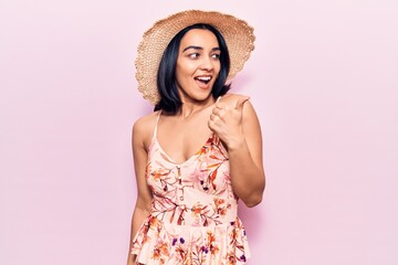 Young beautiful latin woman wearing summer hat pointing thumb up to the side smiling happy with open mouth