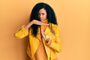 Middle age african american woman wearing wool winter sweater and leather jacket doing time out gesture with hands, frustrated and serious face