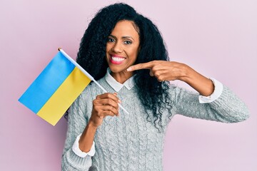 Middle age african american woman holding ukraine flag smiling happy pointing with hand and finger