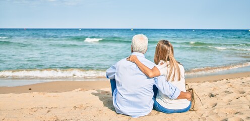 Middle age hispanic couple hugging and sitting at the beach