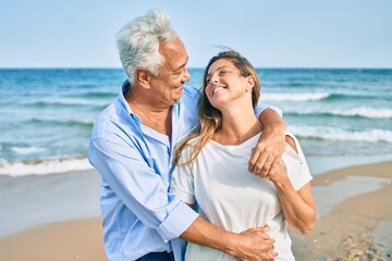 Middle age hispanic couple smiling happy and hugging walking at the beach