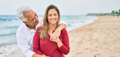 Middle age hispanic couple smiling happy and hugging walking at the beach