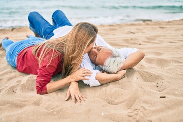 Middle age couple in love lying on the sand at the beach kissing happy and cheerful together