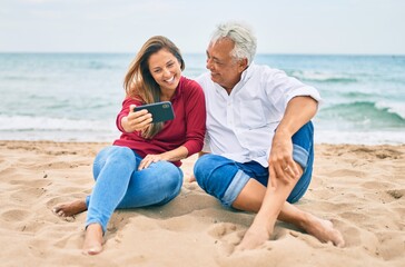 Fototapeta na wymiar Middle age hispanic couple making selfie by the smartphone at the beach.