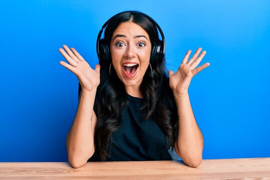 Beautiful brunette young woman listening to music using headphones celebrating crazy and amazed for success with open eyes screaming excited.