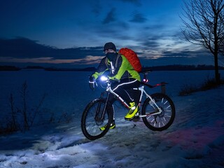 Guy cyclist sits on a MTB during a night ride. City park and light at horizon. MTB riding in slippery snow terrain.