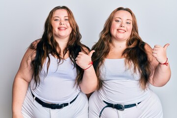 Obraz na płótnie Canvas Plus size caucasian sisters woman wearing casual white clothes smiling with happy face looking and pointing to the side with thumb up.