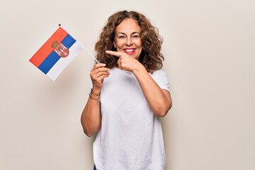 Middle age beautiful patriotic woman holding serbian flag over isolated white background smiling...