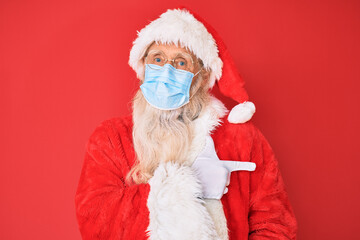 Fototapeta na wymiar Old senior man wearing santa claus costume wearing safety mask smiling cheerful pointing with hand and finger up to the side