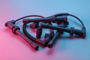 Black ignition wires of a high voltage for spark plugs illuminated with blue and red light. Car...