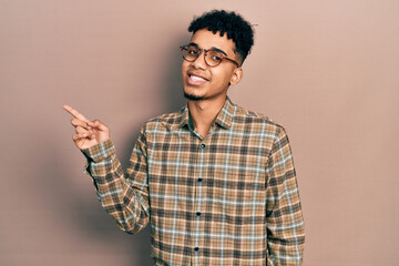 Young african american man wearing casual clothes and glasses smiling happy pointing with hand and finger to the side