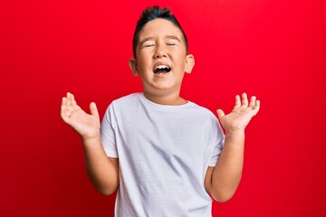 Little boy hispanic kid wearing casual white tshirt celebrating mad and crazy for success with arms raised and closed eyes screaming excited. winner concept