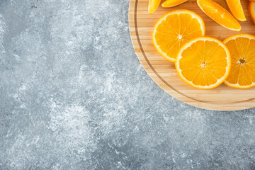 A wooden board full of juicy slices of orange fruit on stone background