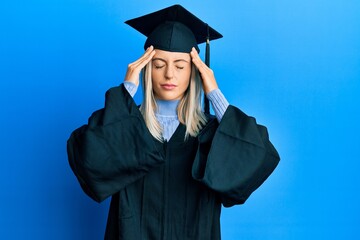 Beautiful blonde woman wearing graduation cap and ceremony robe with hand on head for pain in head because stress. suffering migraine.