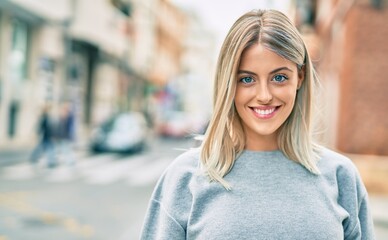 Young blonde girl smiling happy standing at the city.