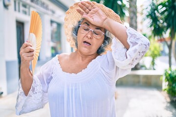 Middle age woman with grey hair using handfan on a very hot day of a heat wave