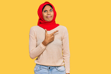 Young african american woman wearing traditional islamic hijab scarf pointing aside worried and...