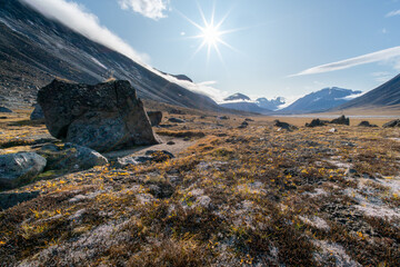 Sun star shines in the sky over remote, wild arctic valley of Akshayuk Pass, Baffin Island on a sunny summer day. Iconic mountains on the distant horizon. © Petr