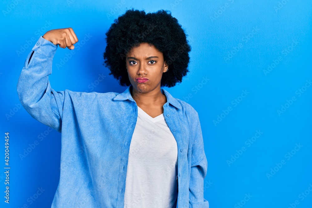 Wall mural young african american woman wearing casual clothes strong person showing arm muscle, confident and 