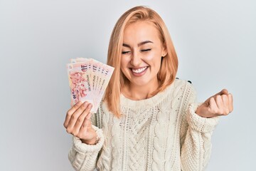 Beautiful caucasian woman holding 10 singapore dollars banknotes screaming proud, celebrating victory and success very excited with raised arm